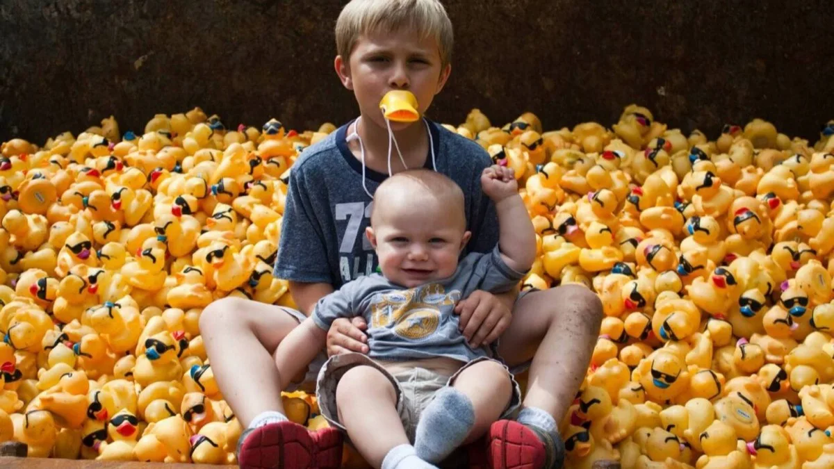 Kids smiling with handfuls of yellow rubber ducks.