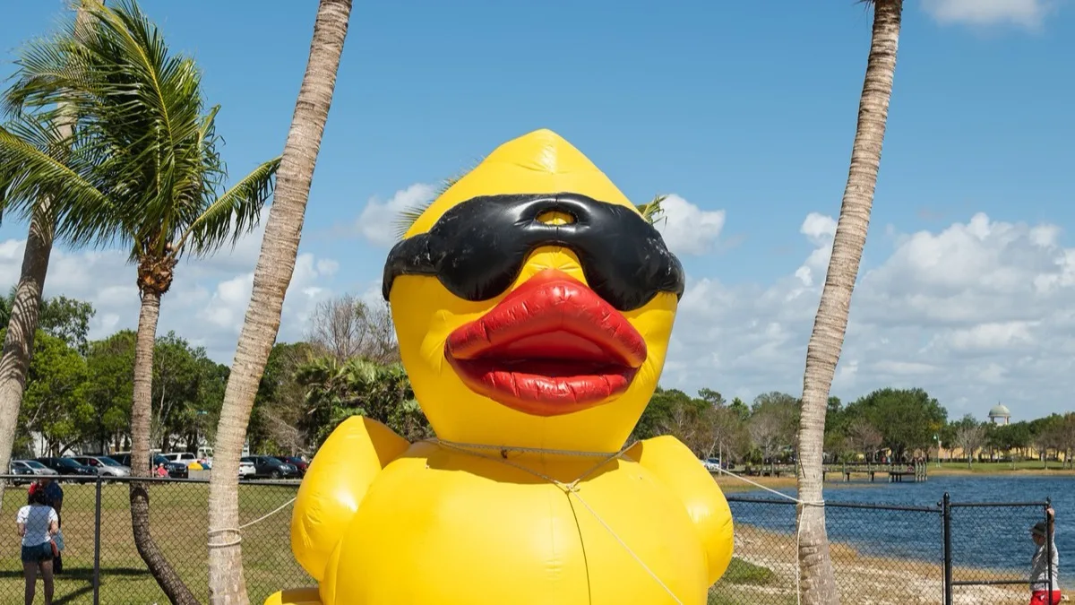 A giant inflatable rubber duck beside palm trees.