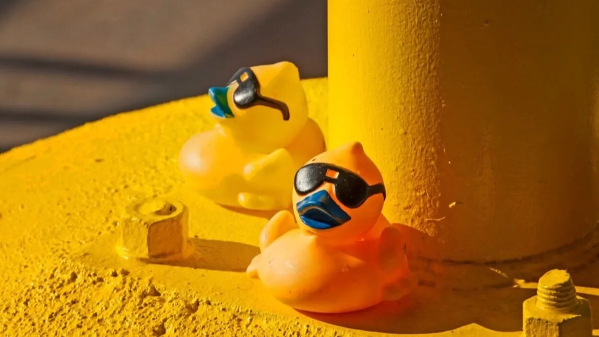 Two yellow rubber ducks on a bright yellow background.