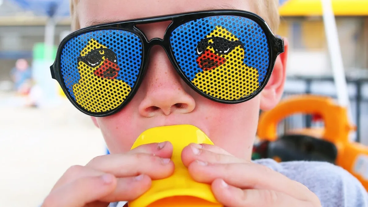 A kid wearing duck sunglasses and blowing a duck call.