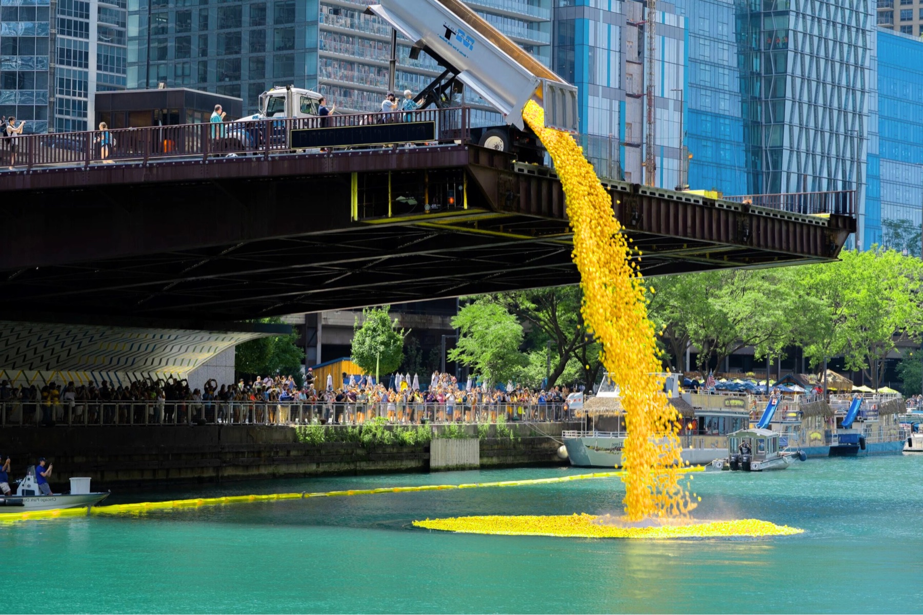 A dump truck pours thousands of yellow rubber ducks off a bridge into the Chicago River while a crowd packs the riverwalk below.