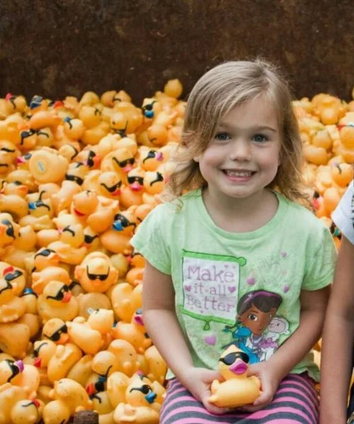 A young girl smiles in front of a pile of rubber ducks.