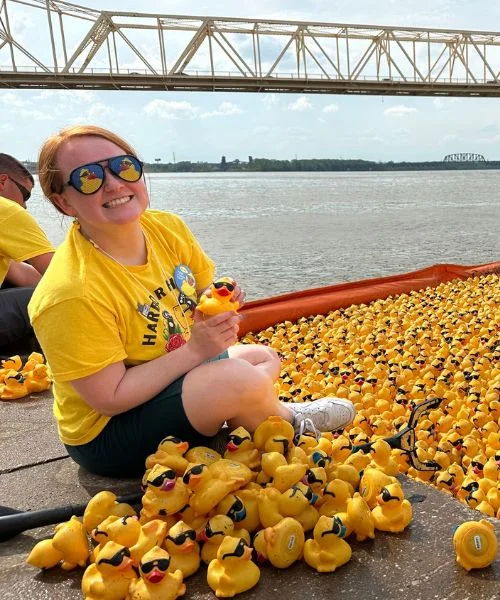 A volunteer in a yellow shirt celebrates beside a river of yellow rubber ducks.