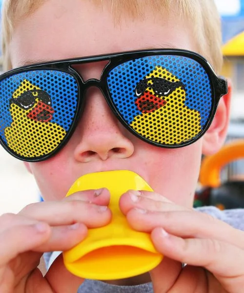 A boy wears duck sunglasses and squeezes a rubber duck.