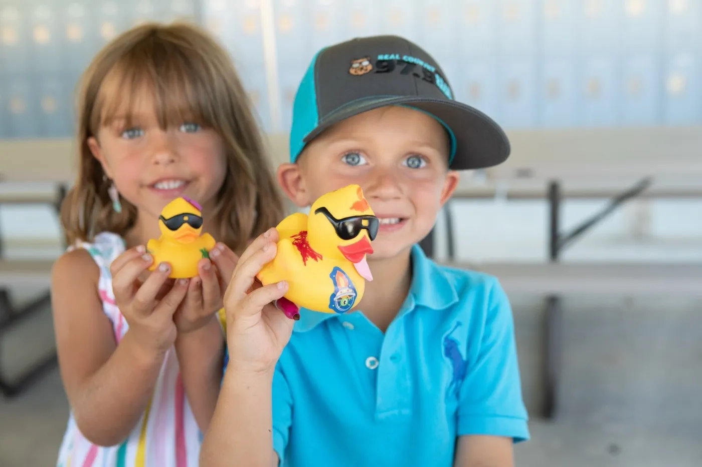 Smiling kids holding yellow rubber ducks beside the water.